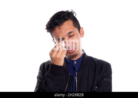 Junger erwachsener junger Mann weint, isoliert auf weißem Hintergrund. Mann weint und wischt seine Tränen mit weißem Taschentuch ab. Stockfoto