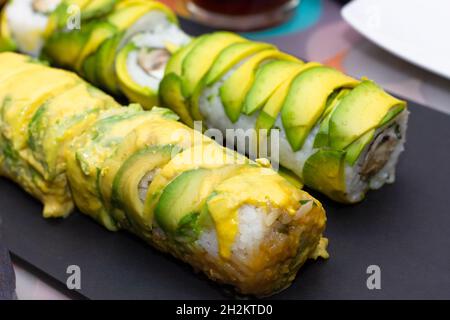 Sushi-Rollen in Avocado verpackt. Nahaufnahme der traditionellen japanischen Speiseteller Stockfoto