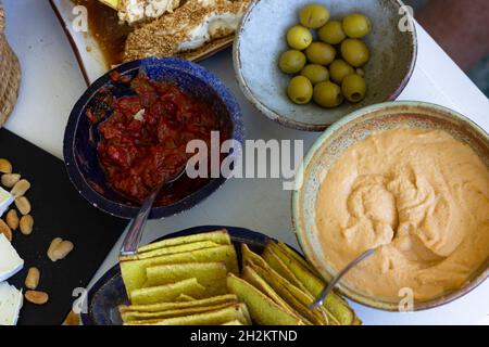 Verschiedene Schüsseln und Snackteller mit Hummus, Oliven, Crackern, Tomatensauce, Käse und Erdnüssen Stockfoto
