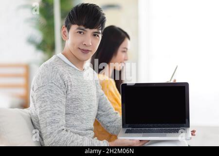 Junges Paar, das Computer zusammen im Wohnzimmer benutzt.Computerbildschirm wird gezeigt. Stockfoto