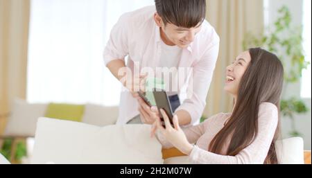 Glückliches junges Paar, das auf der Couch sitzt und auf das Mobiltelefon schaut Stockfoto