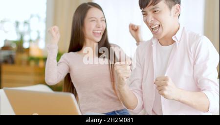 Junges Paar, das zu Hause mit einem Laptop eine Gewinnergeste macht Stockfoto