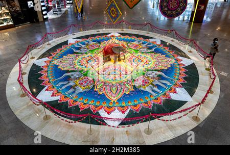 Kuala Lumpur, Malaysia. Oktober 2021. Eine Frau mit Gesichtsmaske geht an einer Kolam-Ausstellung vorbei, einer Form traditioneller indischer Dekorationskunst, die aus Reismehl, weißem Steinpulver und natürlichen Farbpudern im Einkaufszentrum für die bevorstehende Deepavali-Feier in Kuala Lumpur gezeichnet wurde. Kredit: SOPA Images Limited/Alamy Live Nachrichten Stockfoto