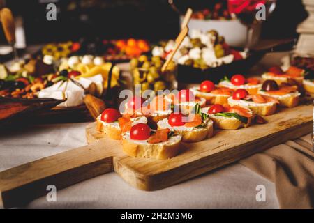 Getrockneten geräucherten Lachs auf den Brotscheiben und Frischkäse-Sandwiches mit Kirschtomaten und Rucola auf dem Tisch Catering Stockfoto