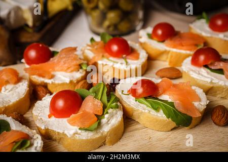 Getrockneten geräucherten Lachs auf den Brotscheiben und Frischkäse-Sandwiches mit Kirschtomaten und Rucola Stockfoto