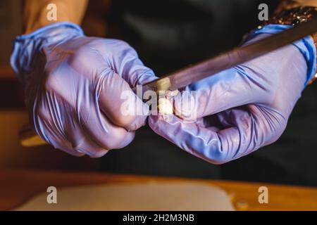 Nahaufnahme der Hände eines unbekannten Mannes oder einer unbekannten Frau, die mit einem Messer den Knoblauch schälen und schneiden Stockfoto