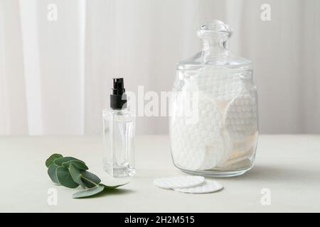 Glas mit sauberen Wattepads und einer Flasche Kosmetikprodukt auf dem Lichttisch Stockfoto