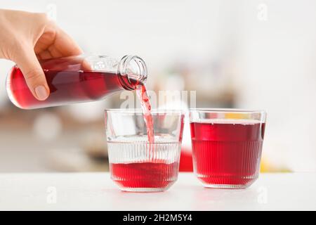 Frau goss aus der Flasche gesunden Saft in das Glas auf dem Tisch im Zimmer, ganz in der Nähe Stockfoto