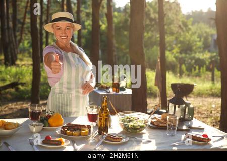 Reife Frau zeigt Daumen-up auf Grillparty am Sommertag Stockfoto