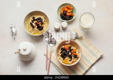 Süßer Haferflocken mit Pflaumen, getrockneten Aprikosen und Mandelnüssen in Schalen auf dem hellen Tisch Stockfoto