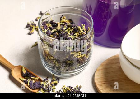 Glas und Schaufel mit getrockneten Schmetterlingsblüten auf hellem Hintergrund Stockfoto