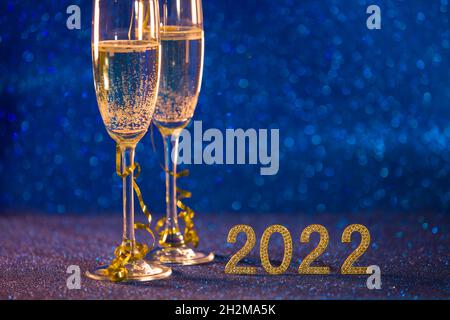 Frohes neues Jahr 2022. Weihnachten und Neujahr Hintergrund mit zwei Tassen, einem Glas Champagner und einem blauen Bokeh-Effekt Hintergrund. Stockfoto