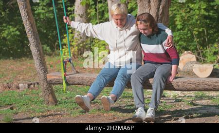 Mutter und Tochter im Teenageralter reiten auf einer Schaukel in der Natur. Stockfoto