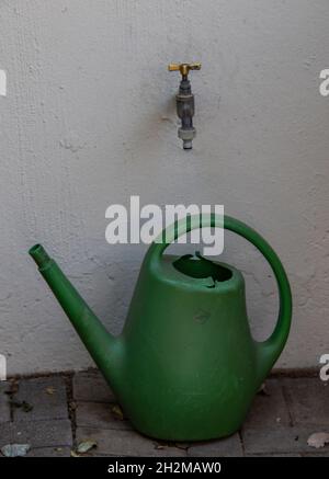 Unter einem geschlossenen Wasserhahn, der an einer Wand montiert ist, steht eine grüne Kunststoffbewässerungsdose Stockfoto