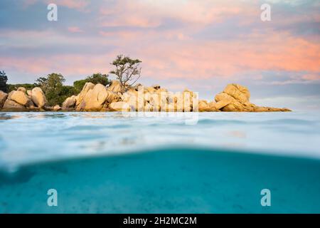 Split-Shot, Over-under-Shot. Halb unterwasser halb Himmel mit türkisfarbenem Meer und einer felsigen Küste, die bei Sonnenuntergang beleuchtet wird. Stockfoto