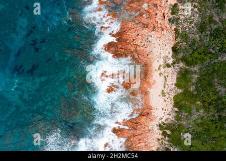 Blick von oben, atemberaubende Luftaufnahme einer grünen und felsigen Küste mit einem weißen Sandstrand, der von einem türkisfarbenen, kristallklaren Wasser umspült wird. Liscia Ruja, Stockfoto