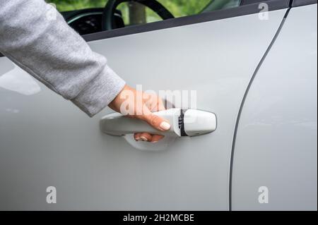 Die Hand einer Frau öffnet die weiße Autotür. Frau öffnet die Autotür. Geschäftsfrau, die die Autotür öffnete und den Griff hielt. Nahaufnahme der Handfahrerin, öffnen Sie die Autotür Stockfoto