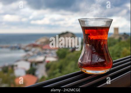 Teetasse-Armudas auf Frauenhand, traditioneller türkischer Tee vor dem Hintergrund des Istanbuler Stadtbildes Sile. Glas Armuda mit Tee Stockfoto