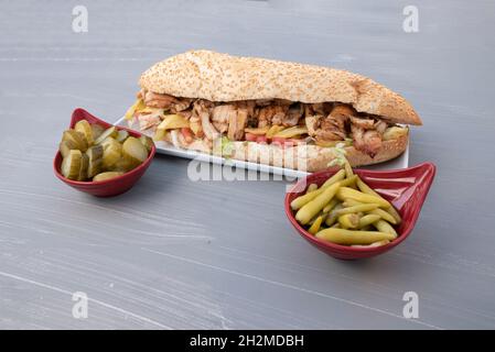 Türkischer Hähnchendöner zwischen Brot, Hähnchenstücken und Brot auf dem Tisch Gurke daneben Stockfoto