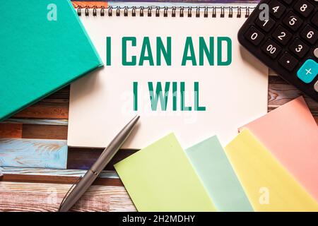 Ich kann und werde auf ein Notizbuch geschrieben, neben farbigen Aufklebern, einem Tagebuch, einem Rechner und einem Stift. Gestreifter Hintergrund Stockfoto