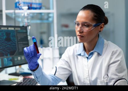 Forscher Biochemiker Arzt analysiert transparenten Vacutainer mit Blut arbeiten an mikrobiologischen Experiment im Krankenhauslabor. Biologin Frau, die mithilfe der Biotechnologie einen medizinischen Impfstoff entwickelt Stockfoto