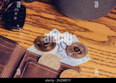 Bitcoin- und Ethereum-Münzen auf einer Lederbörse mit Autoschlüssel auf einer alten Holzplatte. Flaches, hochwertiges Foto mit filmischen Atmosphären Stockfoto