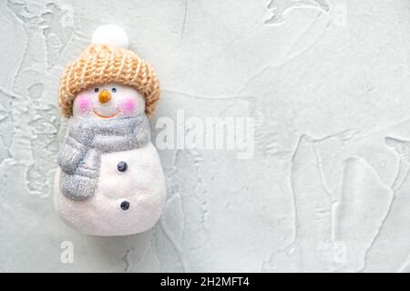 Keramik-Weihnachtsspielzeug - ein niedlicher Schneemann in einem gestrickten Hut mit Pompon und einem Schal auf hellgrünem Hintergrund. Neujahr und weihnachtskonzept. Karte Stockfoto