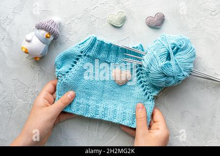 Kinderhände mit einem gestrickten T-Shirt für ein Spielzeug aus türkisfarbenem Baumwollgarn. Die Entwicklung von Feinmotorik. Strickschule. Flach liegend. A Stockfoto