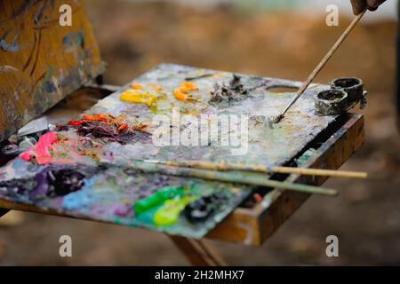 Bild mit geringer Schärfentiefe (selektiver Fokus) mit einem Maler und seiner Farbpalette, während er an einem sonnigen Herbsttag eine Landschaft malte. Stockfoto