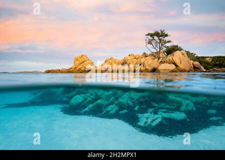 (Selektiver Fokus) Split-Shot, Over-Under-Shot. Halb unterwasser halb Himmel mit türkisfarbenem Meer und einer felsigen Küste, die bei Sonnenuntergang beleuchtet wird. Stockfoto