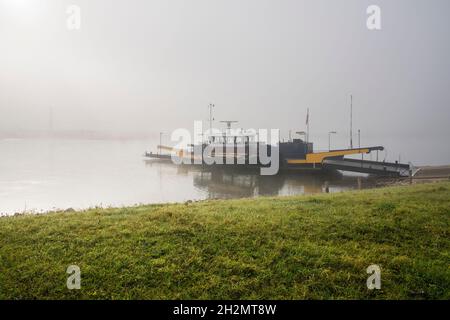 Fähre überquert den Fluss IJssel an einem nebligen Herbstmorgen bei Sonnenaufgang. Stockfoto