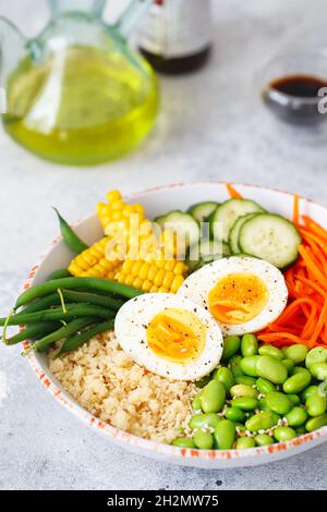 Gesunder Salat mit Couscous, Karotten, Gurken, grünen Bohnen, Sojabohnen, Mais und ein Ei auf grauem Betongrund. Lebensmittel und Gesundheit. Buddha-Schale Sal Stockfoto