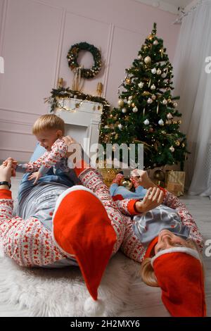 Glückliche Familie in der Nähe von weihnachtsbaum mit Spaß auf dem Boden. Weihnachtsfeier zu Hause. Mama, Papa und Sohn wurden lässig müde. Glückliche Familie lustige spielen Stockfoto