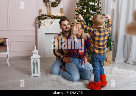 Glückliche Familie in der Nähe von weihnachtsbaum mit Spaß auf dem Boden. Weihnachtsfeier zu Hause. Mama, Papa und Sohn wurden lässig müde. Glückliche Familie lustige spielen Stockfoto