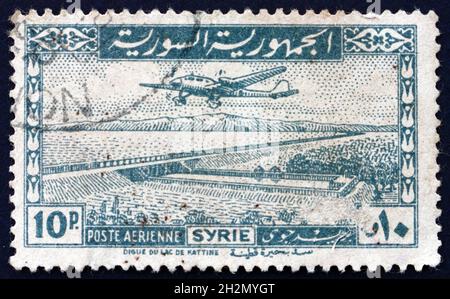 SYRIEN - UM 1947: Eine in Syrien gedruckte Marke zeigt ein Flugzeug über dem Kattineh-Staudamm, um 1947 Stockfoto