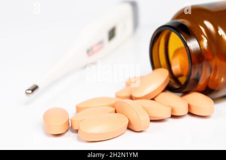 Braune Glasflasche mit gelben Pillen Nahaufnahme und Thermometer auf weißem Hintergrund mit Reflexion Stockfoto