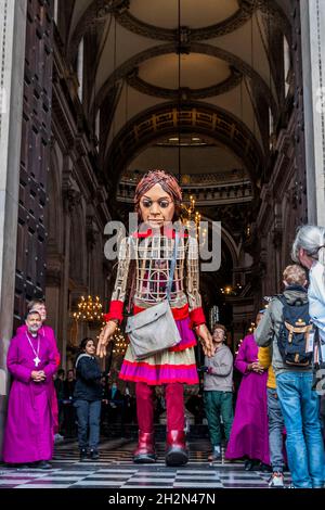 London, Großbritannien. Oktober 2021. Kleriker begrüßen Amal in der St. Paul's Cathedral - die kleine Amal, eine 3.5 Meter große Marionette eines jungen Flüchtlingsmädchen, ist auf einer Reise durch die Türkei und durch Europa unterwegs, um ihre Mutter zu finden. Der Spaziergang ist ein Wanderfestival der Kunst und Hoffnung zur Unterstützung von Flüchtlingen, mit der künstlerischen Leitung von Amir Nizar Zuabi und die Puppe wurde von der Handspring Puppet Company geschaffen. Als Vertreter aller vertriebenen Kinder, viele von ihren Familien getrennt, reist der kleine Amal über 8.000 km und verkörpert die dringende Botschaft „Vergiss uns nicht“. Kredit: Guy Bell/Alamy Live Nachrichten Stockfoto