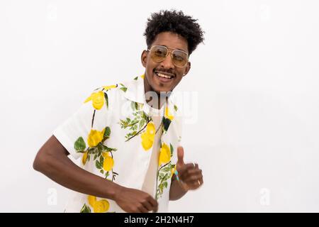 Junger afroamerikanischer Mann in einem floralen Hemd, lächelnd und tanzend auf weißem Hintergrund Stockfoto