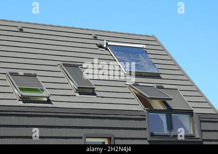 Modernes Hausdach mit Solar Water Heater, Sonnenkollektoren und Oberlichter, schönes neues zeitgenössisches Haus mit Sonnenkollektoren. Offene Dachfenster. Stockfoto