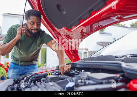 Mann, Der Den Motor Nach Einer Panne Des Autos Ansieht, Ruft Die Automatische Wiederherstellung Auf Dem Mobiltelefon An Stockfoto
