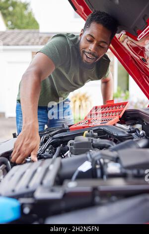 Mann, Der Unter Der Haube Des Auto-Befestigungsmotors Mit Dem Schraubenschlüssel Arbeitet Stockfoto