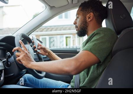 Mann, Der Während Der Fahrt Mit Dem Auto Ein Mobiltelefon Verwendet Stockfoto