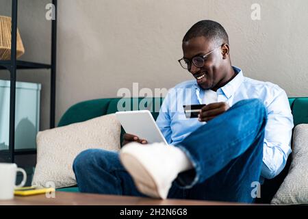 Lächelnder Mann mit digitalem Tablet und Kreditkarte, während er zu Hause auf dem Sofa sitzt Stockfoto