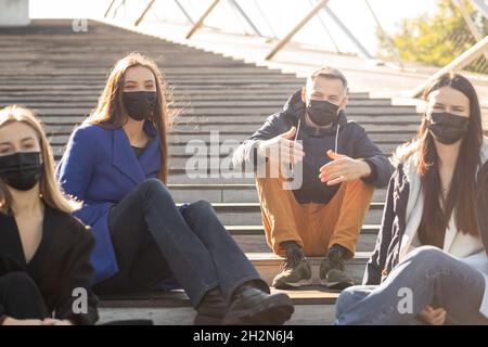 Neu ist das normale Konzept. Junge Menschen unterhalten sich und haben Spaß mit schützenden Gesichtsmasken während des Pandemieausbruchs am frühen Herbstsonntag. Hell lebhaft b Stockfoto