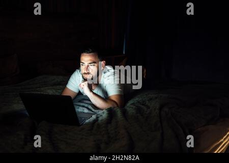 Nachdenklicher Mann mit Laptop, während er zu Hause auf dem Bett lag Stockfoto