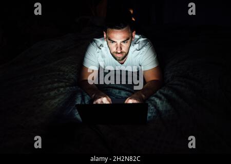 Ernsthafter Mann mit Laptop im Schlafzimmer Stockfoto