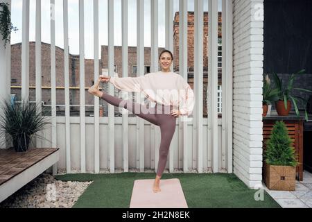 Lächelnde Frau, die auf der Terrasse Utthita Hasta Padangusthasana posiert Stockfoto