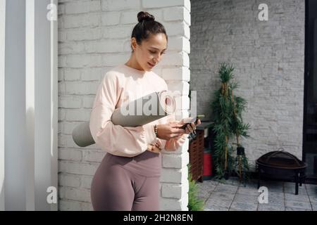 Frau mit mittlerem Erwachsenen und Yogamatte mit Mobiltelefon auf der Terrasse Stockfoto
