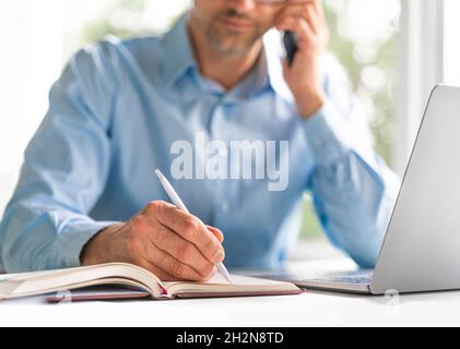 Reifer Geschäftsmann, der im Büro an der Rezeption Tagebuch schreibt Stockfoto