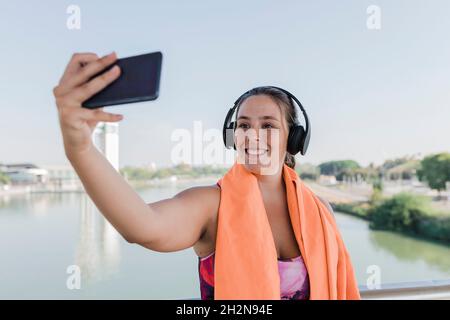 Die Sportlerin lächelt, während sie Selfie über das Mobiltelefon nimmt Stockfoto